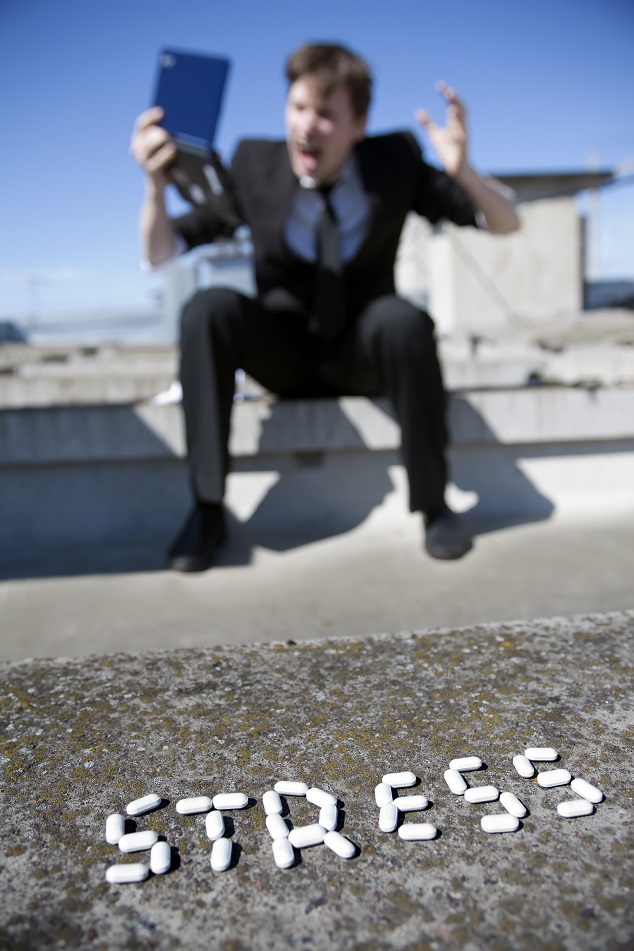 Stress Conceptual image - businessman with netbook screaming and suffering from stress. On foreground word "stress" is written with tablets. Focus on foreground.